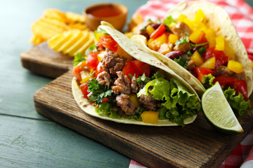 Homemade beef burritos with vegetables, potato chips on cutting board, on wooden background