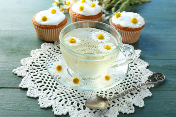 Cup of chamomile tea with chamomile flowers and tasty muffins on color wooden background