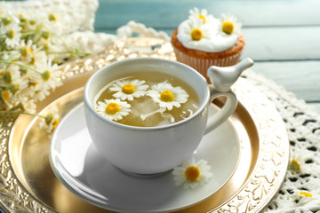 Cup of chamomile tea with chamomile flowers and tasty muffins on tray, on color wooden background
