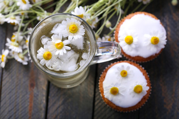 Fototapeta na wymiar Cup of chamomile tea with chamomile flowers and tasty muffins on color wooden background