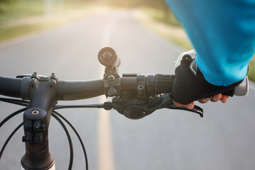 Hands in gloves holding handlebar of a bicycle on road.