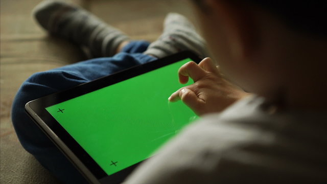 Child using a digital tablet PC with green screen, back view
