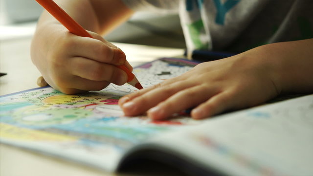 Child hands paints a orange pencils on a paper
