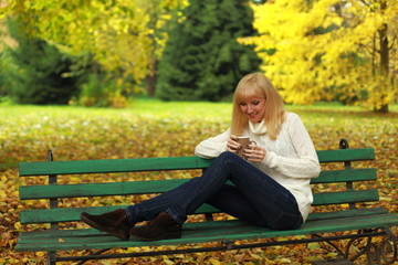 Girl with a cup of coffee on a bench in the park in autumn