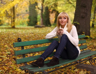 Girl with a cup of coffee on a bench in the park in autumn
