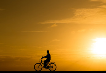 Silhouette man riding the bike at sunset