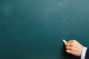 Hand mit Kreide an gr&uuml;ner Tafel