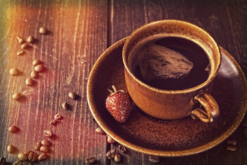 Black coffee in an ancient mug with strawberry on a wooden background