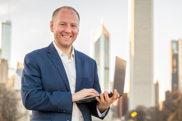 Businessman with laptop in front of office buildings
