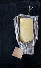 Mature cheddar cheese wrapped in rustic paper with a blank label.