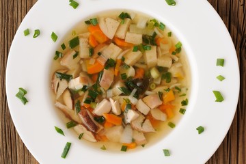 Porcini mushrooms soup with scallion in white plate on wooden ba
