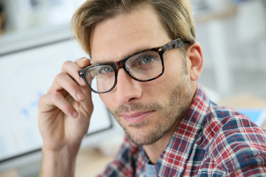 Trendy guy with eyeglasses sitting in office in front of desktop computer