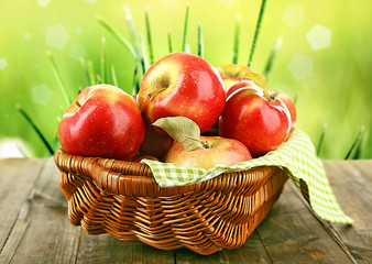 Wicker basket of red apples with napkin on bright background