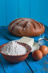 Baking bread in rural kitchen - dough recipe ingredients eggs, flour, butter and whisk, screen on vintage wood table from above