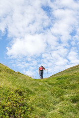 senda verde / Hombre de espaldas subiendo por un sendero de montaña, cielo azul con nubes blancas