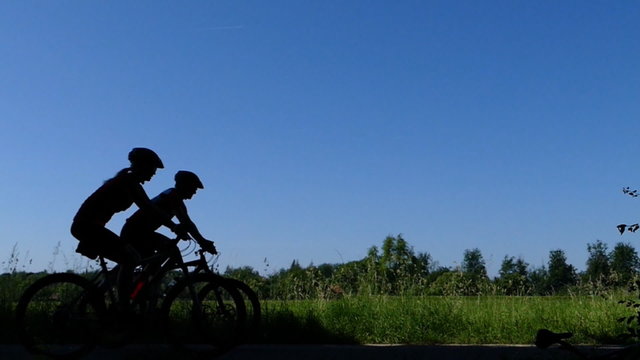 Mann und Frau fahren mit dem Fahrrad als Silhouette vorbei, in Zeitlupe