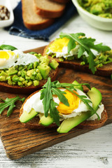 Tasty sandwiches with egg, avocado and vegetables on wooden background
