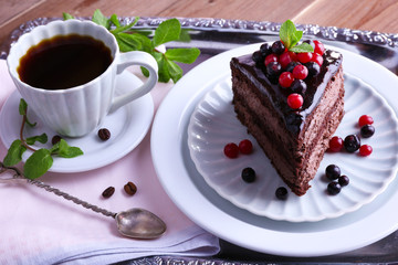Delicious chocolate cake with berries and cup of coffee on table close up