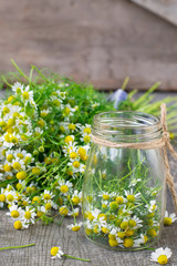 chamomile flowers in a glass jar on a wooden background