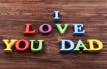 Inscription I LOVE YOU DAD made of colorful letters on wooden background