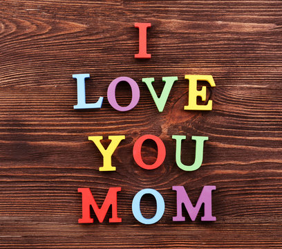 Inscription I LOVE YOU MOM made of colorful letters on wooden background