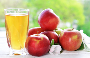 Glass of apple juice and apples on wooden table, on nature background