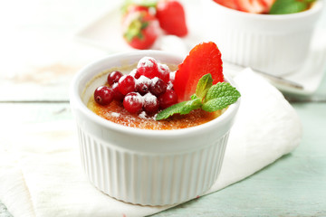 Creme brulee dessert with fresh strawberry berries on napkin, on color wooden background