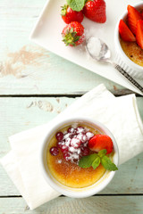 Creme brulee dessert with fresh strawberry berries on napkin, on color wooden background