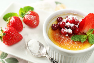 Creme brulee dessert with fresh strawberries and mint leaves, on color wooden background