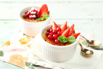 Creme brulee dessert with fresh strawberries and mint leaves, on color wooden background