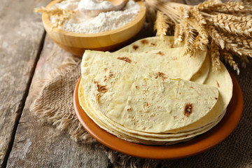 Stack of homemade whole wheat flour tortilla on plate, on wooden table background