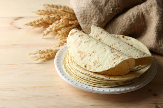 Stack of homemade whole wheat flour tortilla on plate, on wooden table background