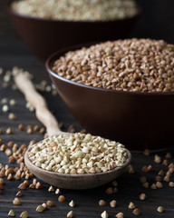 Green and brown buckwheat in ceramic bowls on a wooden surface
