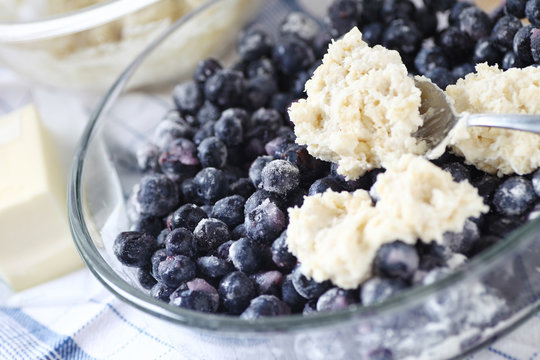 Spooning biscuit dough onto a bowl of sugared blueberries