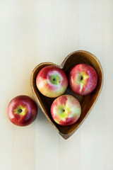 Apples in the wooden heart shape plate on the table, close up