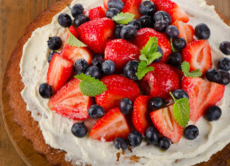 Strawberry and blueberry  cream cake on  a wooden background.