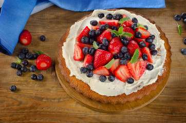 Strawberry and blueberry  cream cake on a rustic wooden backgrou
