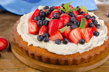 Fresh berry  cream cake on  wooden background.