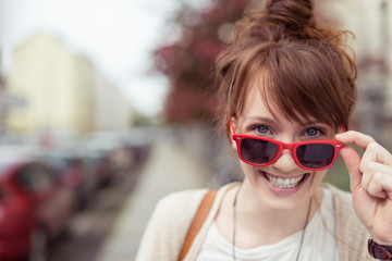 frau schaut lachend über ihre rote sonnenbrille