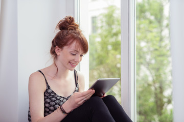 frau sitzt am fenster und schaut auf ihr tablet