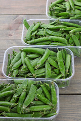 fresh green peas in a plastic container on a wooden background