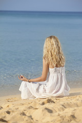 Fototapeta na wymiar young woman with beautiful blonde hair meditating in sea on beach