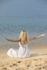 Fototapeta na wymiar young woman with beautiful blonde hair meditating in sea on beach