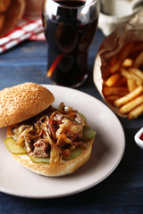 Tasty burger and french fries on plate, on wooden table background. Unhealthy food concept