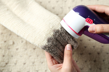 Female hands with Wool shaver on wool sweater background