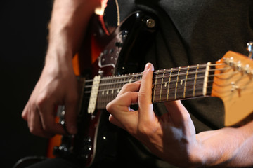 Fototapeta na wymiar Young man playing on electric guitar on dark background