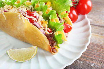 Tasty taco with vegetables on plate on table close up
