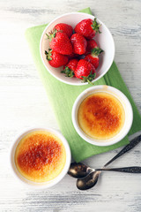 Creme brulee dessert with fresh strawberry berries on napkin, on color wooden background