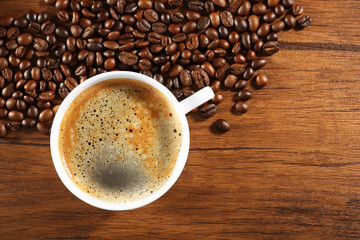 Cup of fresh coffee with beans on table, closeup