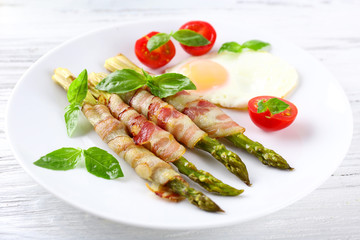 Dish of asparagus with bacon and egg in plate on table, closeup